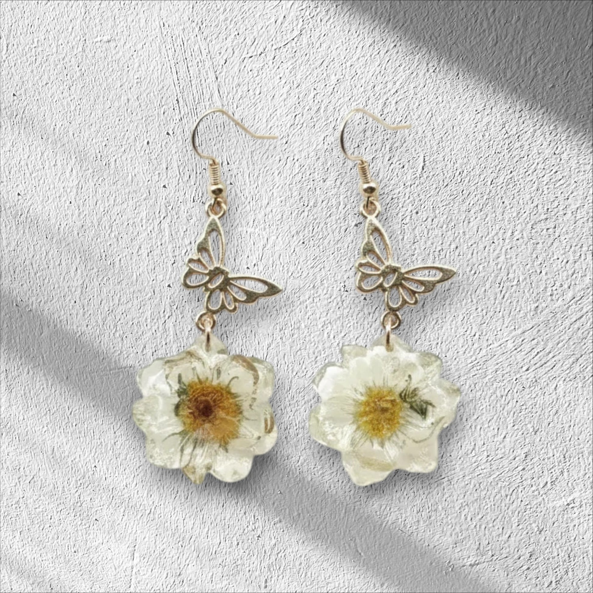 Alyssa's House gold-tone butterfly earrings featuring cream pressed flowers in a whimsical vintage style.