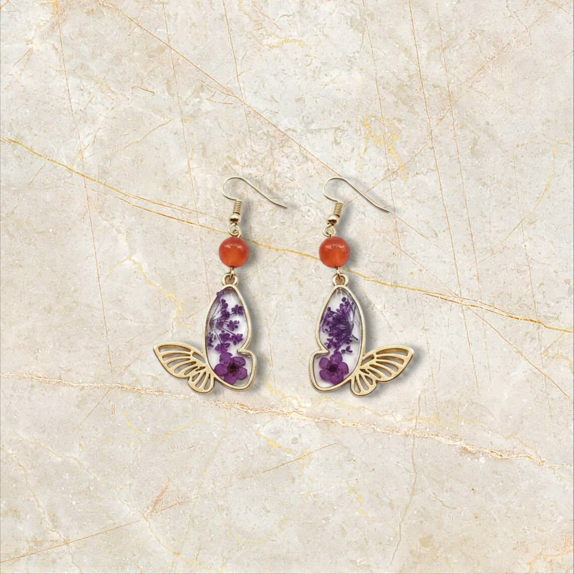 Alyssa's House gold-tone butterfly earrings featuring purple pressed flowers and red bead accents.