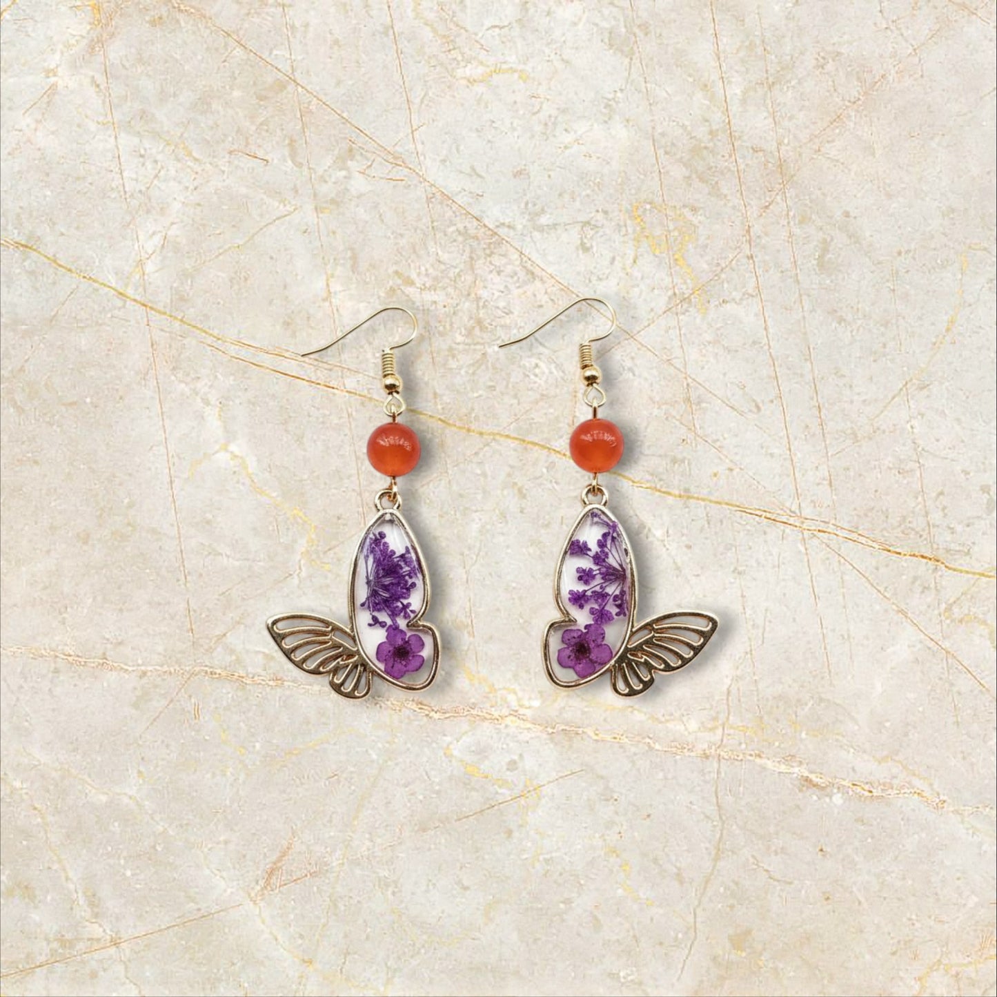 Alyssa's House gold-tone butterfly earrings featuring purple pressed flowers and red bead accents on hook wires.