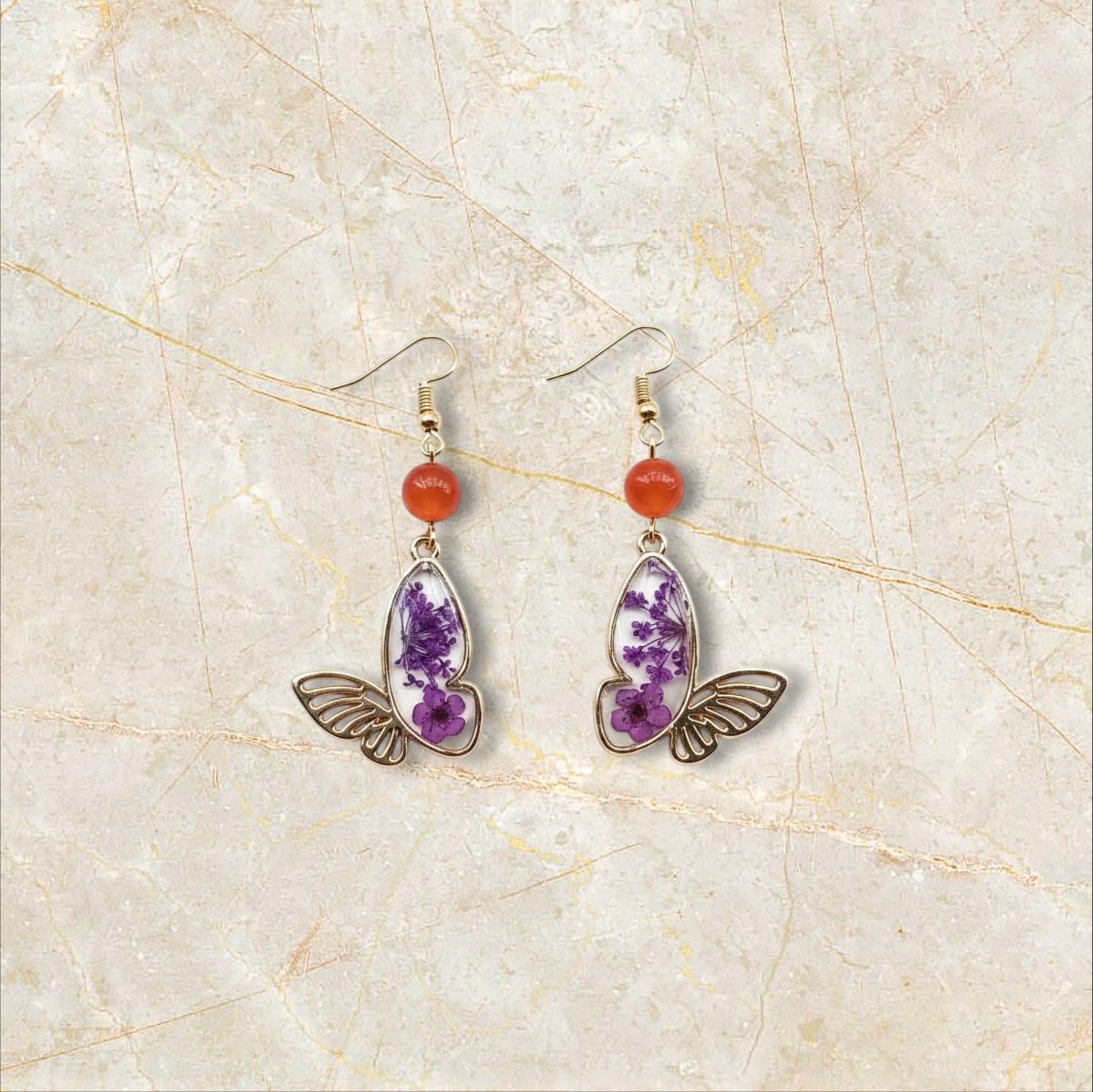 Alyssa's House gold-tone butterfly earrings featuring purple pressed flowers and red bead accents on hook wires.