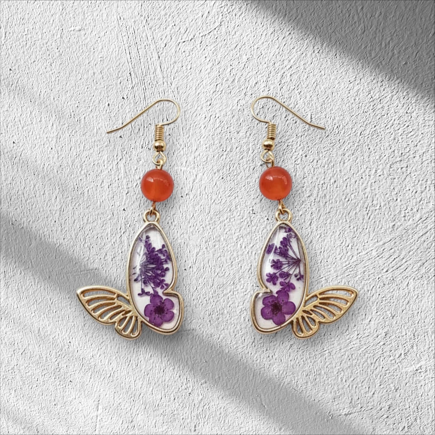 Alyssa's House gold-tone butterfly earrings featuring purple pressed flowers and red bead accents.