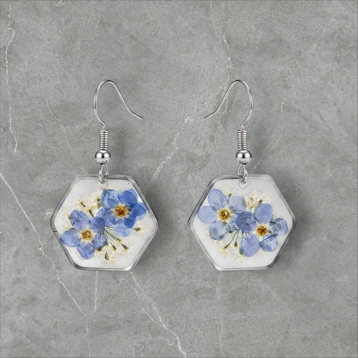 Alyssa's House hexagon resin earrings featuring pressed blue forget-me-not flowers in silver-tone wire frames.