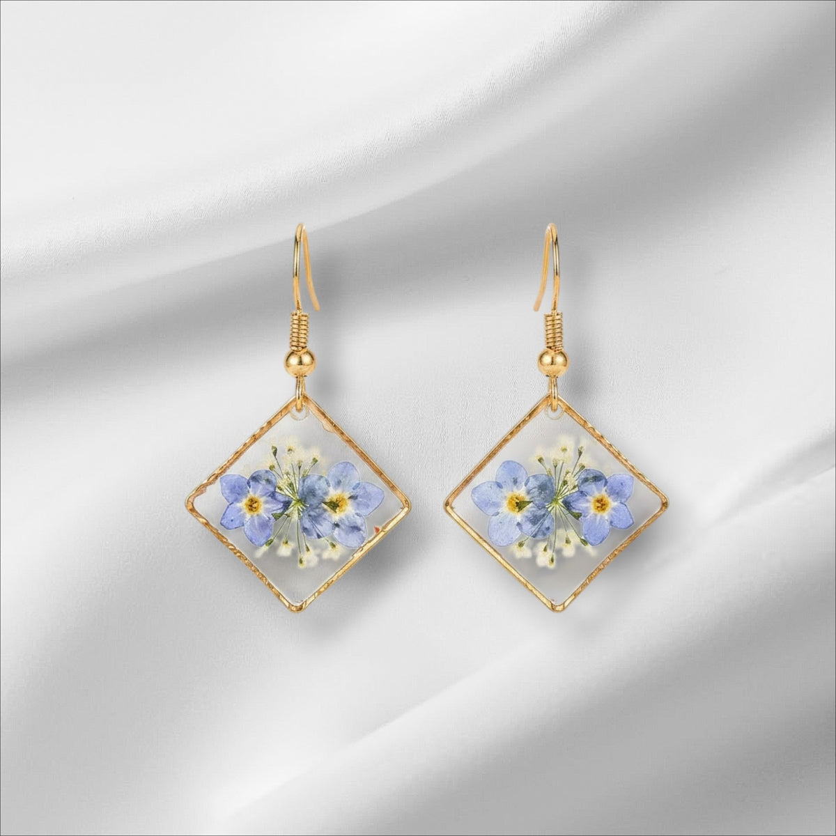 Alyssa's House diamond-shaped resin earrings featuring pressed blue forget-me-not flowers in a gold-tone frame.