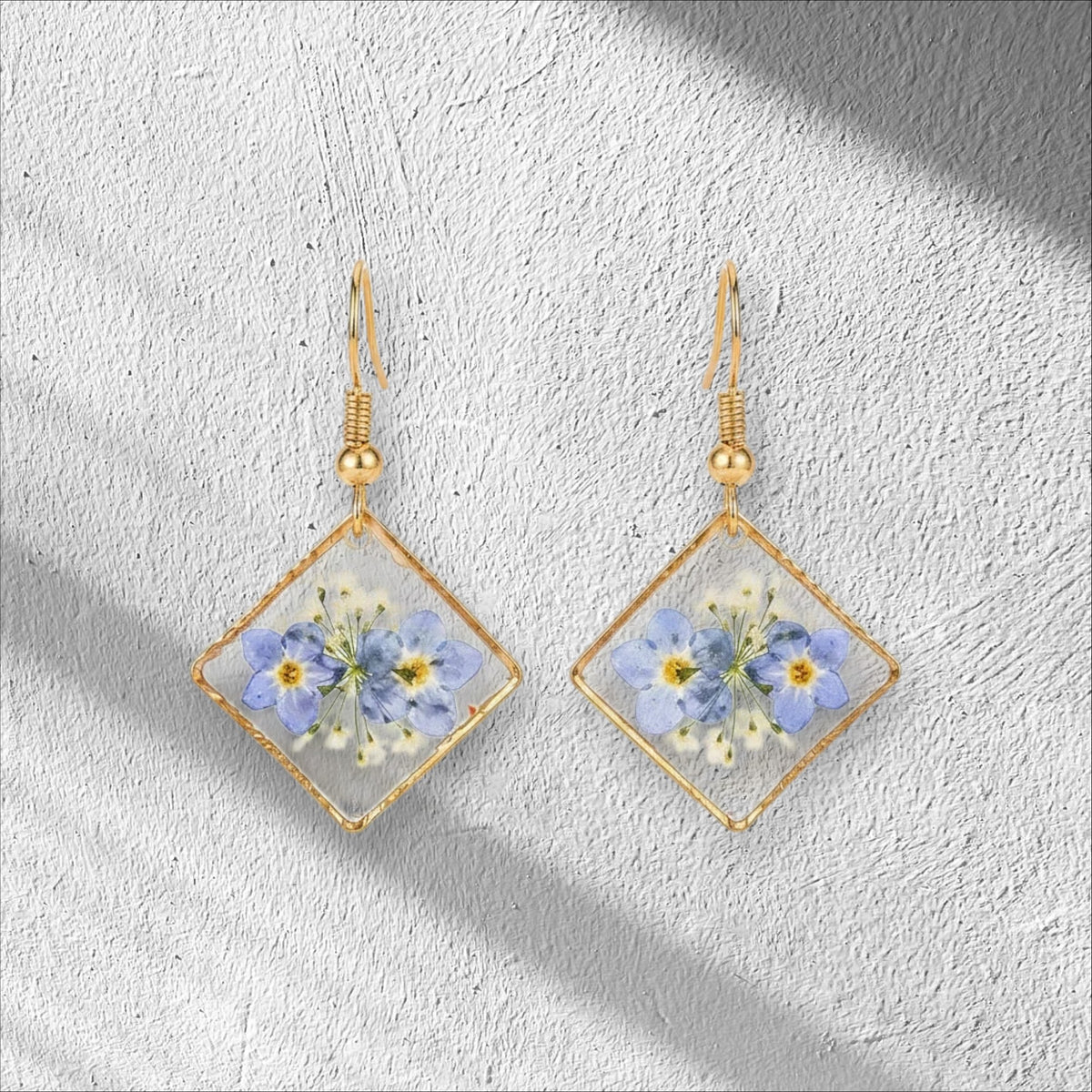Alyssa's House diamond-shaped resin earrings featuring pressed blue forget-me-not flowers in a gold-tone frame.