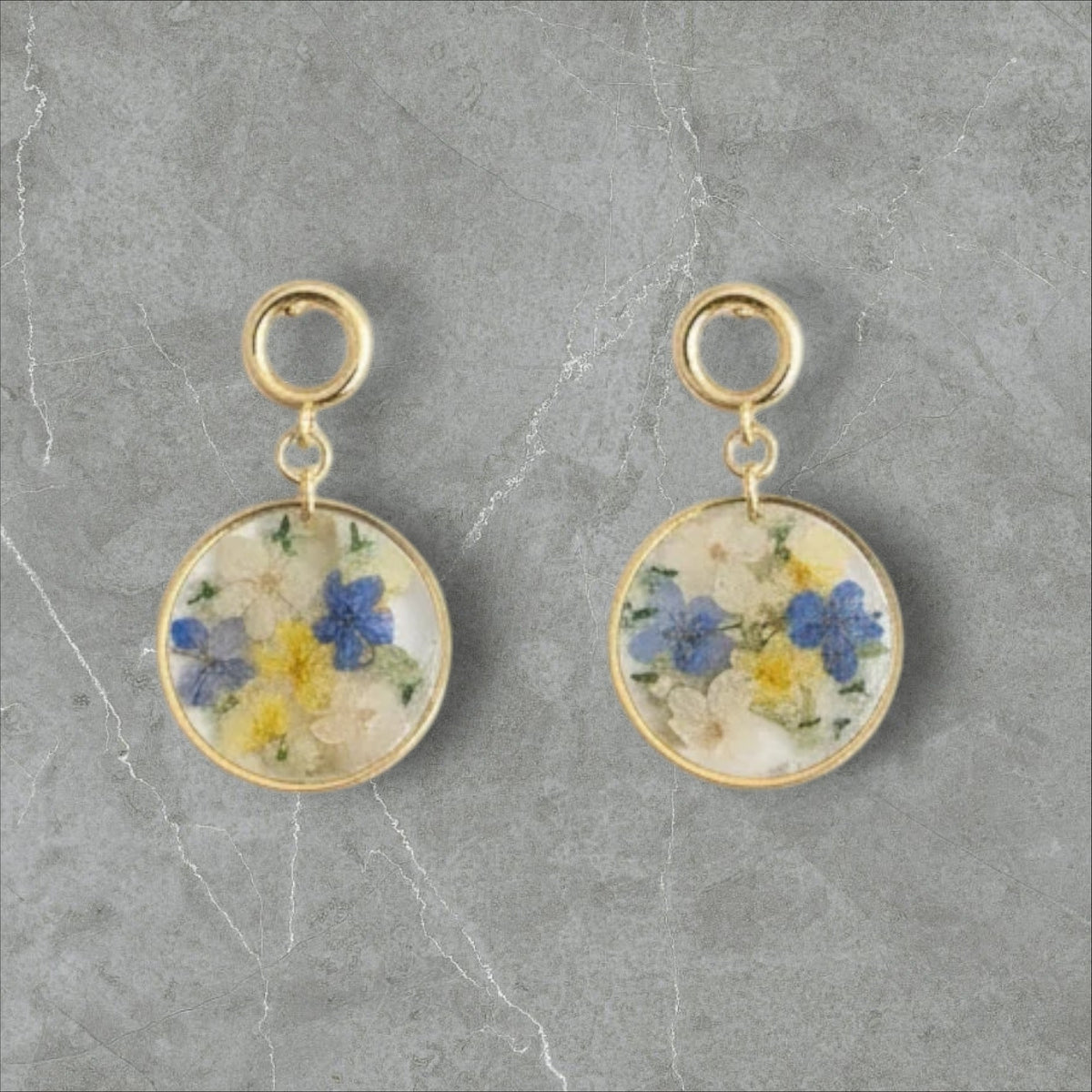 Alyssa's House round resin earrings featuring pressed blue and yellow flowers with gold-tone drop hooks.