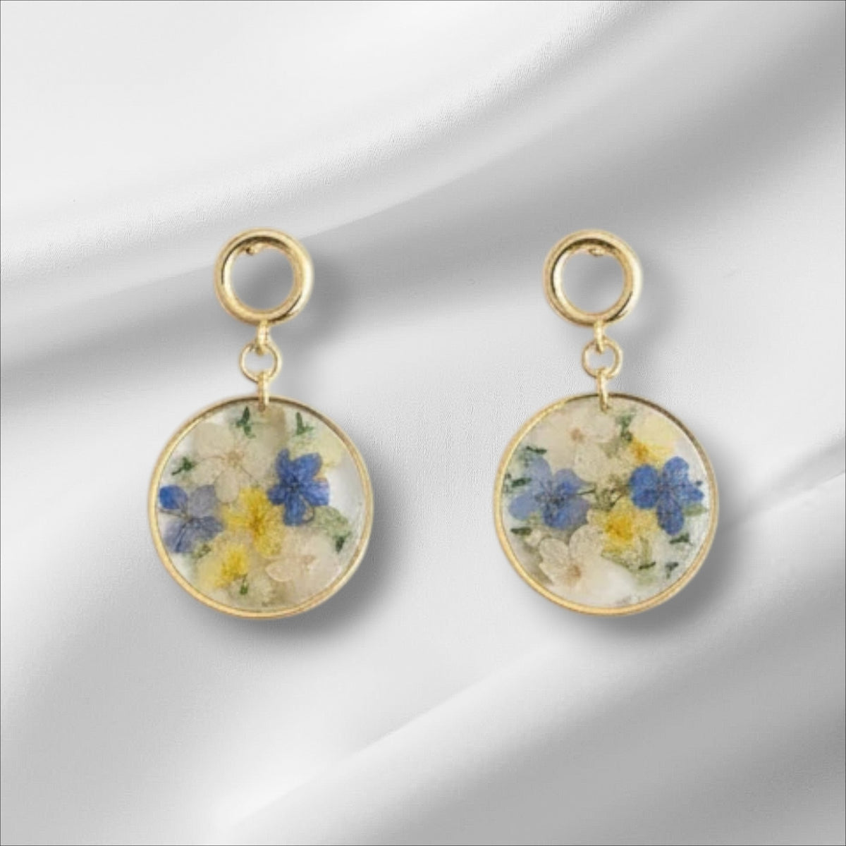 Alyssa's House round resin earrings featuring pressed blue and yellow flowers with gold-tone drop hooks.